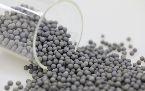 Grey-blue mineral–alloy ceramic balls spilling from a glass beaker (media maker's photo)