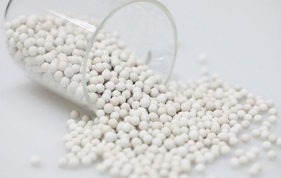 Off-white mineral ceramic balls made with maifan stone and pearl powder spilling from a glass beaker (media maker's photo)